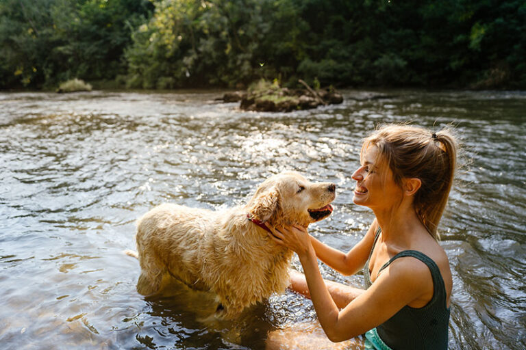 Photo of a smiling young woman and her dog sitting in the river